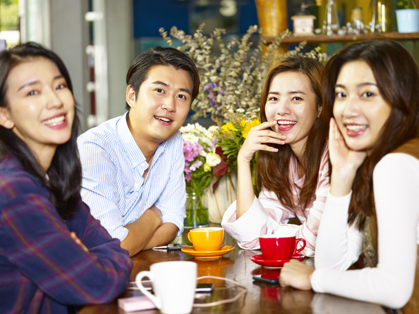 група з чотирьох щасливих азіатських молодих дорослих чоловік і жінка дивиться на камеру посміхаючись під час збору в кав'ярні
. - Фото, зображення