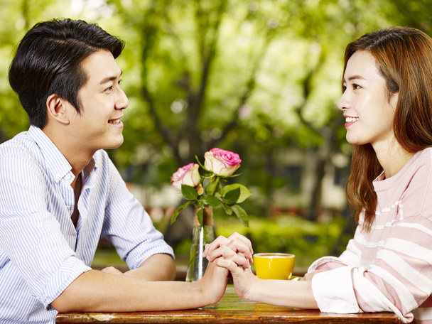 nuori aasialainen mies ja nainen istuu kasvotusten pitäen toisiaan kädestä pitäen kahvilassa
. - Valokuva, kuva