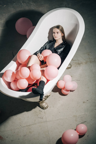 woman relax in bath. party balloons in bubbles bath tub. fashion model in autumn coat. hygiene and spa treatment. having fun in bathroom. Inspiration and wellness concept. health care and beauty. - Foto, immagini