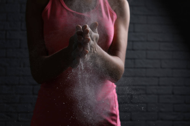 Young woman applying chalk powder on hands against brick wall - Fotó, kép