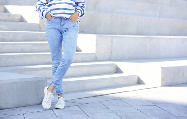 屋外階段の近くに立ってスタイリッシュなジーンズの流行に敏感な若い女性 - 写真・画像