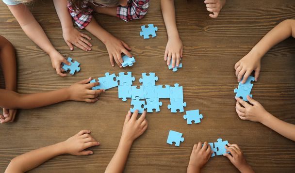 Top view of little children playing puzzle together at table, focus on hands. Unity concept - Fotó, kép