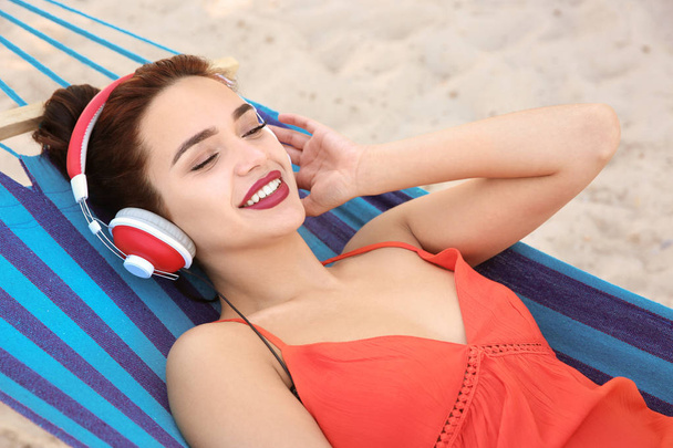 Молода жінка слухає музику в зручному гамаку на узбережжі
 - Фото, зображення