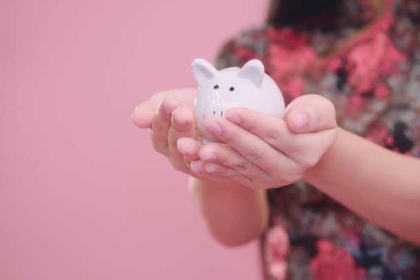 Little Piggy bank in young women hand on pink blackground, money savings concept. - Foto, afbeelding