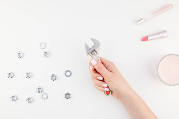 Creative image of woman hand with pastel manicure polish holding spanner with copy space nuts and cosmetics isolated white background in minimalism style. Repair or improvement feminism concept - Photo, Image