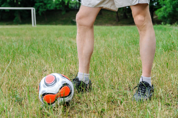 Las piernas de los hombres están en la hierba. Hay una pelota de fútbol al lado.
. - Foto, Imagen