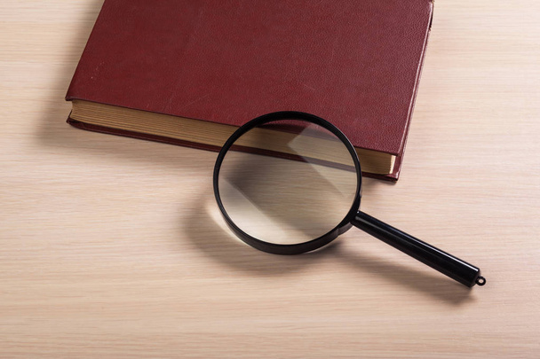 Magnifying glass and book o the wooden background - Foto, imagen