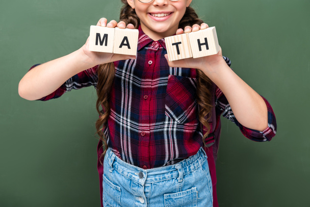 黒板近く単語数学の木製キューブを保持している小学生の画像をトリミング - 写真・画像
