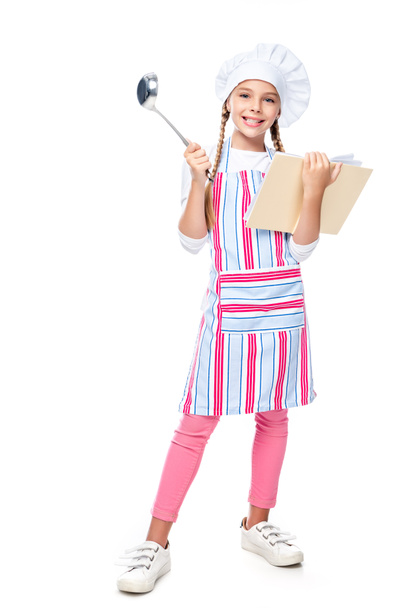 smiling schoolchild in costume of chef holding ladle and cookbook isolated on white - Photo, Image