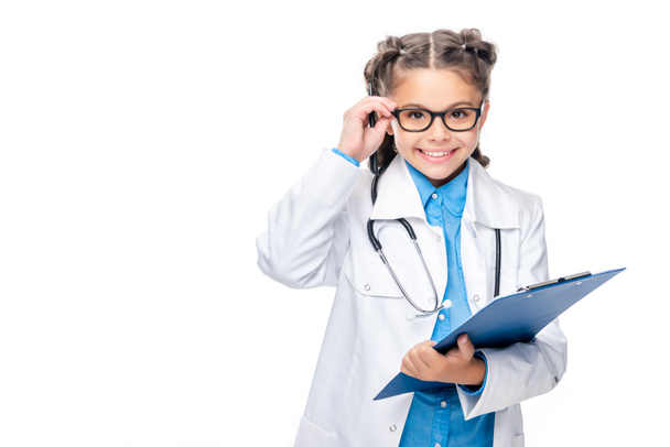 écolier en costume de médecin tenant presse-papiers et lunettes touchantes isolé sur blanc
 - Photo, image