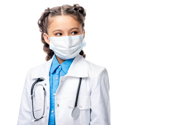 escolar en máscara médica mirando hacia otro lado aislado en blanco
 - Foto, Imagen