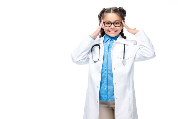 schoolchild in costume of doctor touching head and looking at camera isolated on white - Foto, Imagem