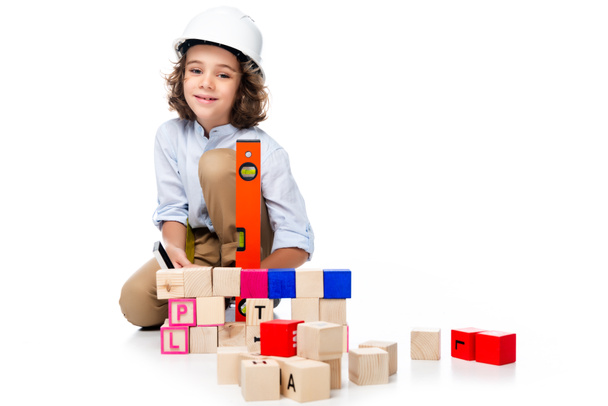 écolier en costume d'architecte et casque mesurant des cubes en bois avec niveau d'esprit isolé sur blanc
 - Photo, image