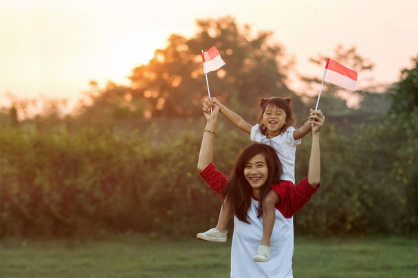 mother and daughter raising flag of indonesia - Fotó, kép