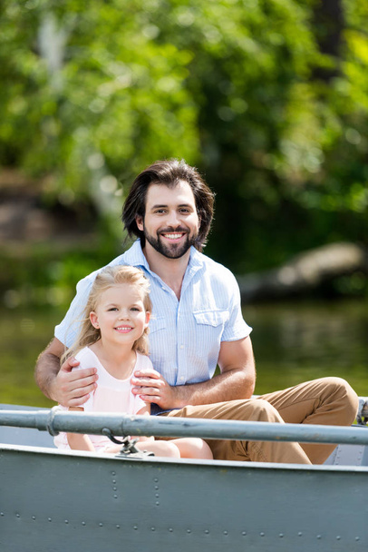 happy father and daughter sitting in boat on lake at park and looking at camera - Photo, Image