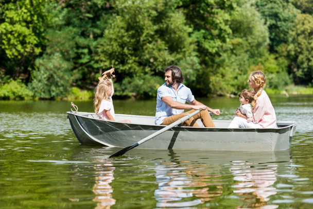 вид сбоку красивой молодой семьи катающейся на лодке по реке в парке в солнечный день
 - Фото, изображение