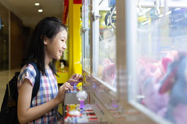 Asiática chica jugando garra juego o gabinete atrapa a la muñeca en uno de los centros comerciales
 - Foto, imagen
