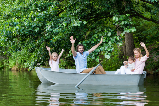happy young family with raised hands riding boat on lake at park - Foto, Bild