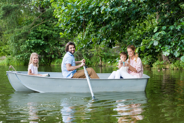 side view of smiling young family spending time together in boat on lake at park - 写真・画像