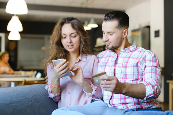 Młoda kobieta szczęśliwa i człowiek za pomocą smartfona i debetowej w kawiarni. - Zdjęcie, obraz