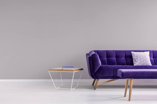 Pillow on a stylish, vibrant purple settee and a diamond shape, side table in a gray living room interior with place for a floor lamp. Real photo. - Fotó, kép