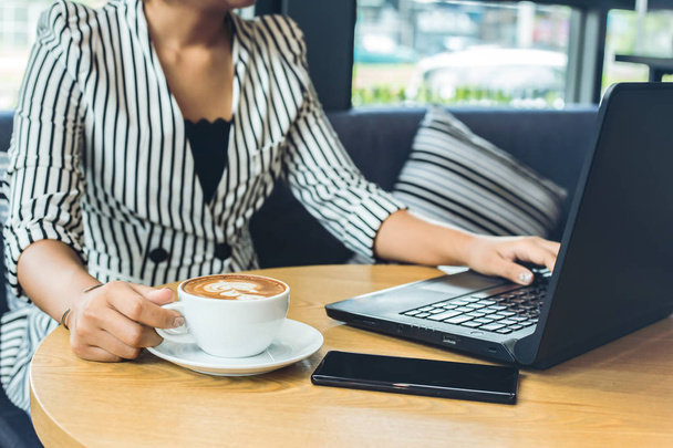 businesswomen working with laptop and hand catch cup of coffee. A mobile phone is on the table near the laptop. - 写真・画像