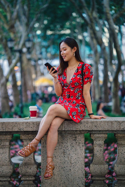 young woman in red dress with smartphone sitting on street  - Photo, Image