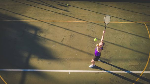 Aerial image of a young woman playing tennis on a tennis court shot from overhead with a drone - Photo, image
