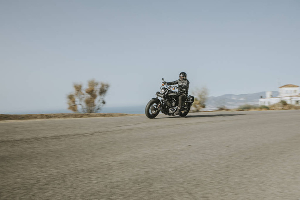 Man in black clothes riding an American motorcycle fast in a road in the mountain, with blue sky in the background. - Foto, Bild
