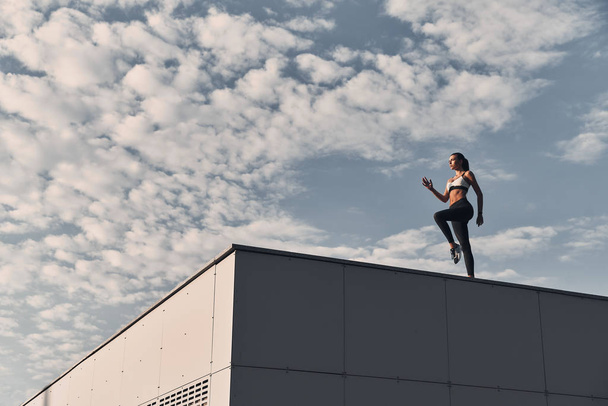 full length of muscular young woman in sports clothing exercising on building roof  - Foto, Imagem