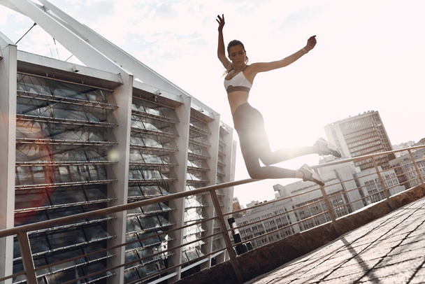 full length of sportive Caucasian woman in sport leggings jumping from railings outdoors  - Photo, image