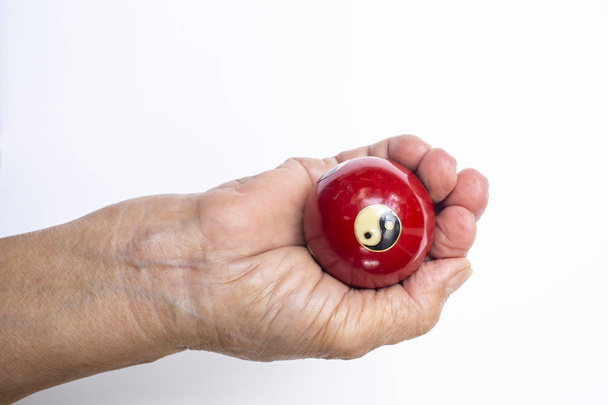 Die rechte Hand der Seniorin hält ein schwarz-weißes Yin Yang religiöses Symbol auf rotem Ball in Taoismus isoliert auf weißem Hintergrund - Foto, Bild