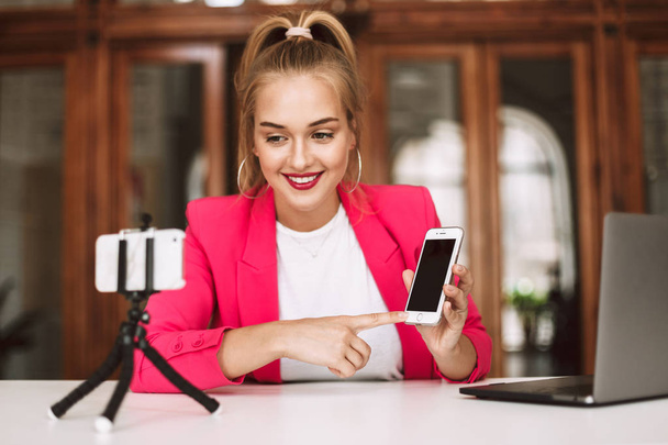 Досить усміхнена дівчина в рожевій куртці щасливо записує відео нового смартфона для відеоблогу
 - Фото, зображення
