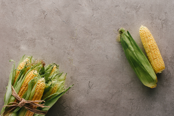 top view of fresh corn cobs tied with rope and one corn apart on grey concrete surface - Photo, Image