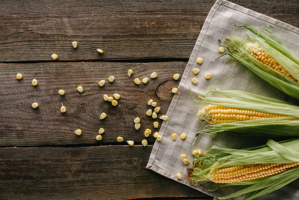 top view of fresh raw corn cobs on linen and grains wooden tabletop - Φωτογραφία, εικόνα