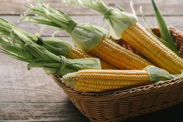 close up view of raw corn cobs in basket on wooden surface - Zdjęcie, obraz