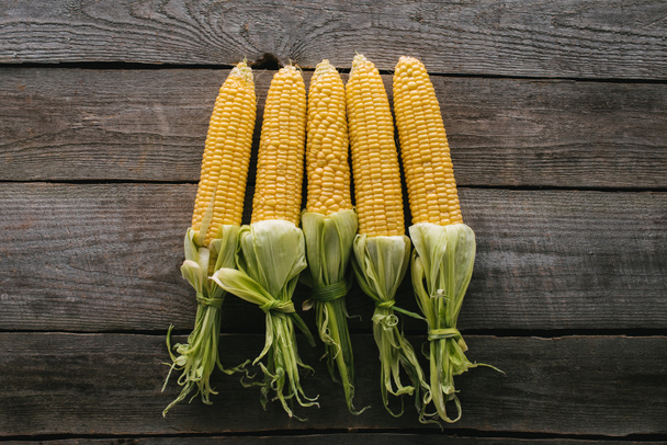 top view of arranged fresh raw corn cobs on wooden tabletop - Foto, Bild