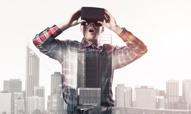Young man with virtual reality headset or 3d glasses over cityscape background - Фото, зображення