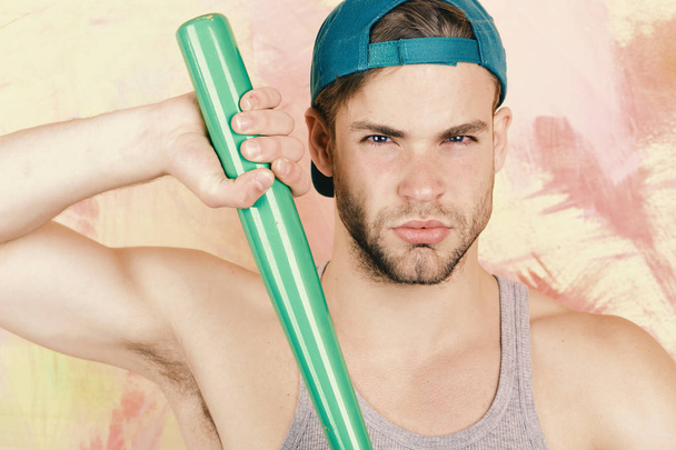 Man in cyan green cap on colorful background. Guy in grey tank top holds bright green bat, closeup - Foto, afbeelding