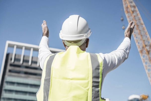Engineer man in helmet and jacket controlling outdoor construction site - Фото, изображение