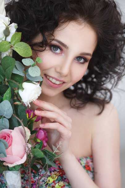 Mysterious smiling brunette girl looks out from behind a bush of roses. - Фото, изображение
