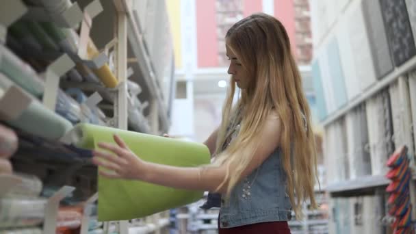 Νεαρή γυναίκα παίρνει από ράφι σε ένα κατάστημα ένα ρολό ταπετσαρία - Πλάνα, βίντεο