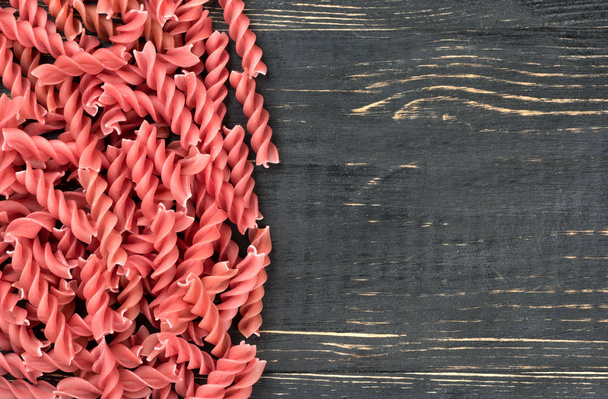 Κόκκινο ωμά ζυμαρικά fusilli σε ένα άδειο φόντο ξύλινη - Φωτογραφία, εικόνα
