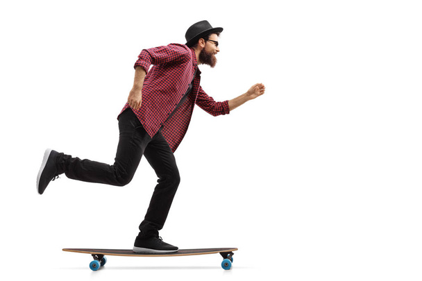 Full length profile shot of a hipster riding a longboard isolated on white background - Photo, image