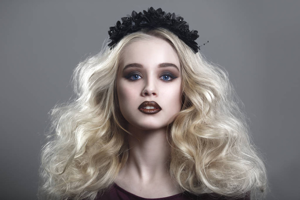 Beauty portrait of a beautiful young blonde woman with gothic make-up and decorative wreath on a gray background. - Valokuva, kuva