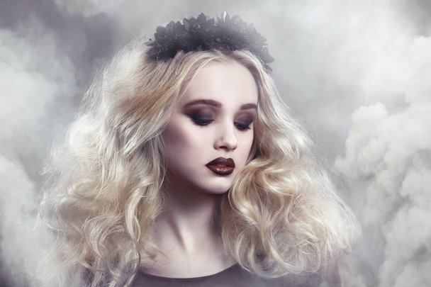 Beauty portrait of a beautiful young blonde woman with gothic make-up and decorative wreath in a puff of smoke. - Zdjęcie, obraz
