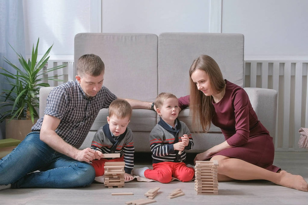 Family mom, dad and two twin brothers play together building out of wooden blocks on the floor. - Photo, image