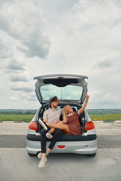 Beautiful young couple taking selfie in car trunk - 写真・画像