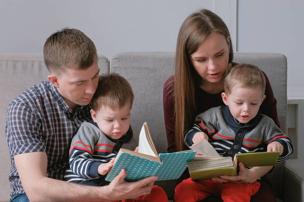 Family mom, dad and two twin brothers read books sitting on the sofa. Family reading time. - Foto, Imagen