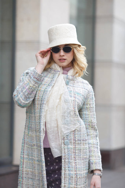 A beautiful stylish blond woman in a coat and hat and sunglasses on a city street. - Foto, immagini